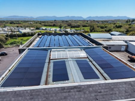 Aerial view of the 140-panel solar PV arrays on the flat roof and forecourt canopy at Centra Glenbeigh, Co. Kerry, with Dingle Bay behind